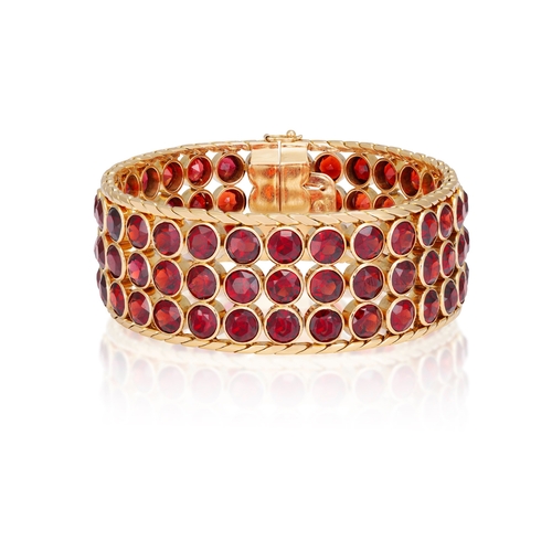 38 - A GARNET AND GOLD BRACELET, CIRCA 1950  The wide band collet-set with circular-cut garnets, to fine-... 