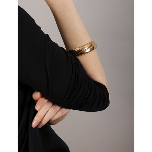 7 - A GOLD 'TRINITY' BANGLE, BY CARTIER  Composed of three interlocking polished 18K tri-coloured gold b... 