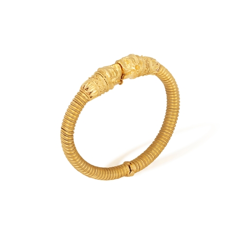 79 - A 22K GOLD BANGLE  Of spring design, each terminal with opposing stylised Chimera heads, to a reeded... 