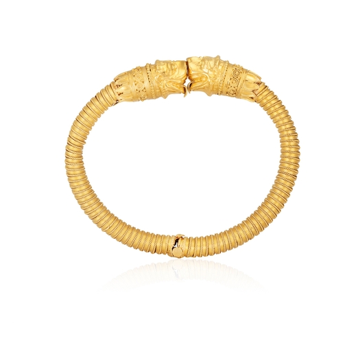 79 - A 22K GOLD BANGLE  Of spring design, each terminal with opposing stylised Chimera heads, to a reeded... 