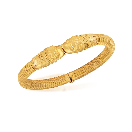 79 - A 22K GOLD BANGLE  Of spring design, each terminal with opposing stylised Chimera heads, to a reeded... 