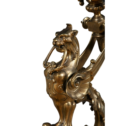 41 - A PAIR OF BRASS FIRE DOGS,   in the form of winged griffins, perched on pierced brackets. 53cm high