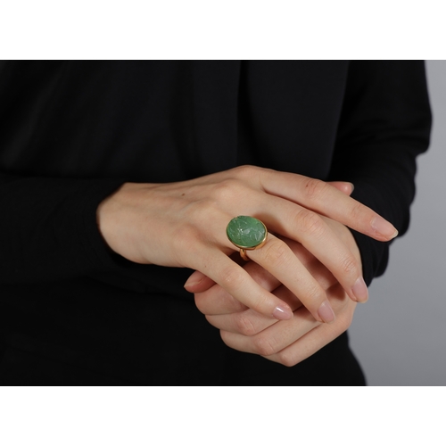 135 - AN EMERALD RING  Of foliate design, the oval-shaped carved cabochon emerald weighing approximately 3... 