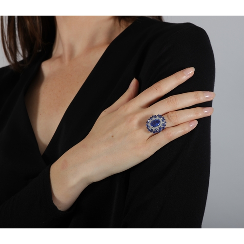 187 - A SAPPHIRE AND DIAMOND CLUSTER RING  The elongated oval-shaped sapphire within a four-claw setting, ... 