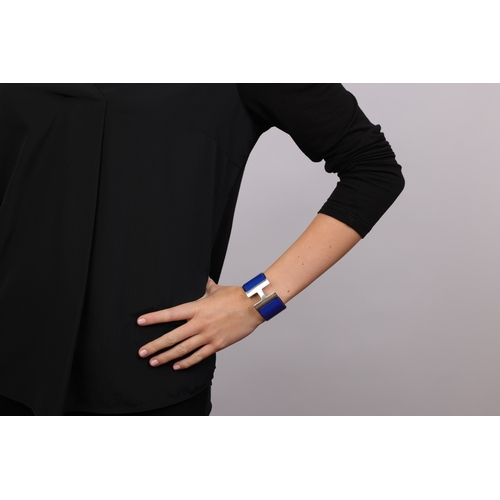 117 - HERMÈS: A 'CLIC CLAC H' BRACELET  The bangle with applied blue enamel, centring an H clasp, signed H... 