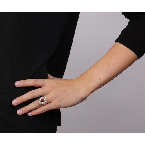 82 - A RUBY AND DIAMOND RING  Of cluster-design, centring an oval-shaped ruby, within a double-border of ... 