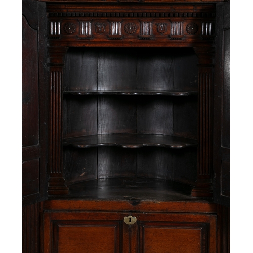 529 - A GEORGE III OAK CORNER CABINET,  the swan neck pediment with rosette terminals, twin fielded panel ... 