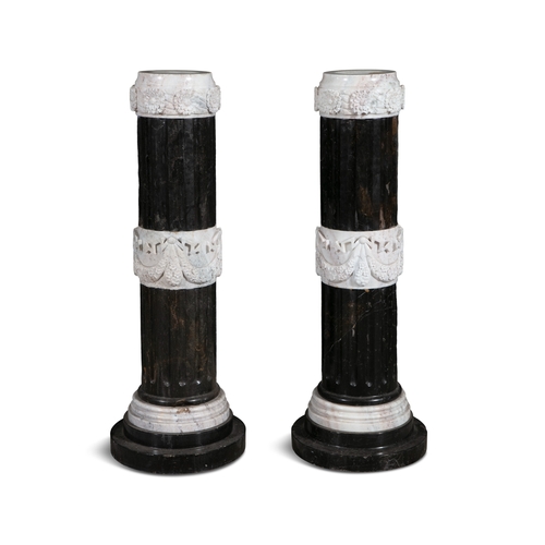 687 - A PAIR OF BLACK MARBLE PEDESTALS OF NEO-CLASSICAL DESIGN SUPPORTING CONFORMING URNS,  the urns carve... 