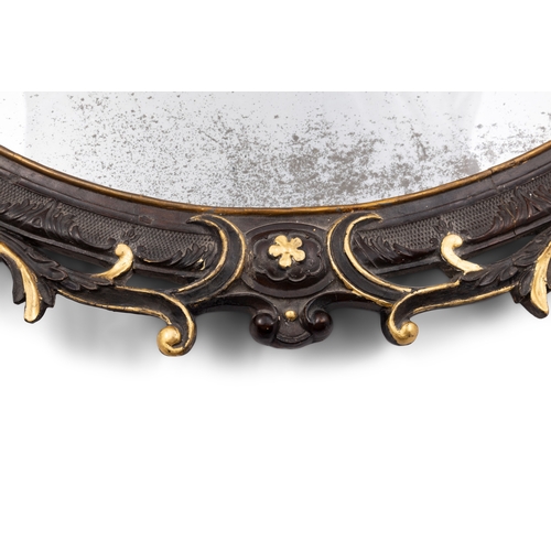 115 - A CONTINENTAL EBONISED AND GILTWOOD OVAL MIRROR,   the frame carved with foliage, C-scrolls and flow... 