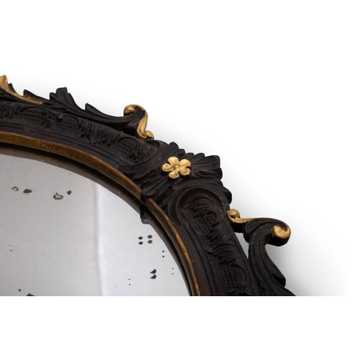 115 - A CONTINENTAL EBONISED AND GILTWOOD OVAL MIRROR,   the frame carved with foliage, C-scrolls and flow... 