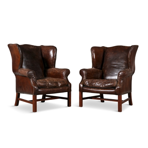 65 - A PAIR OF GEORGE III STYLE BROWN LEATHER WING BACK ARMCHAIRS,  each with loose cushions, raised on s... 