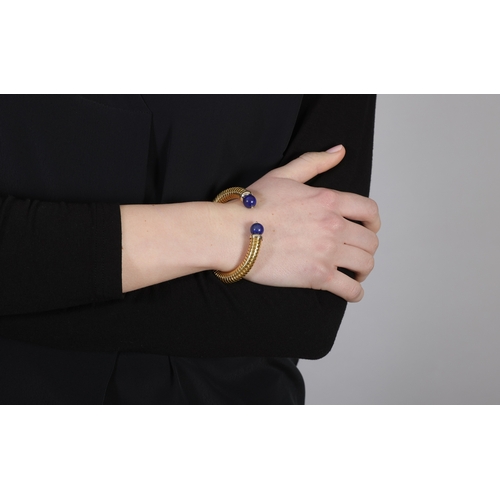 200 - A LAPIS LAZULI AND 18K GOLD BANGLE  Of spring tubogas design, set with lapis lazuli bead terminals, ... 