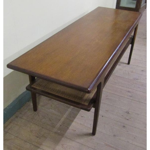 623 - A 1970s teak low table of rectangular form with a caned under tier shelf, supported on straight tape... 