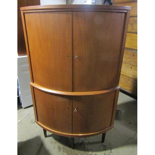 634 - A 1970's teak standing bow front corner cupboard with upper and lower shelves enclosed by hinged doo... 