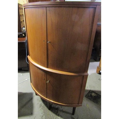 634 - A 1970's teak standing bow front corner cupboard with upper and lower shelves enclosed by hinged doo... 