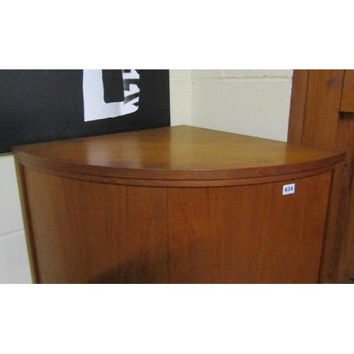 634 - A 1970's teak standing bow front corner cupboard with upper and lower shelves enclosed by hinged doo... 