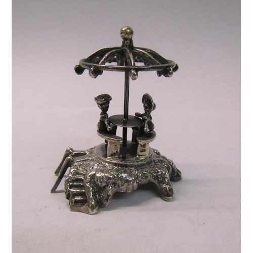 164 - A late 19c silver miniature figure group of two people sitting at a table on a mound under a parasol... 