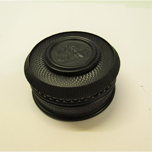 69 - A Vulcanite ebony circular box with circular pictorial classical panel to the lid, 7cm diam.