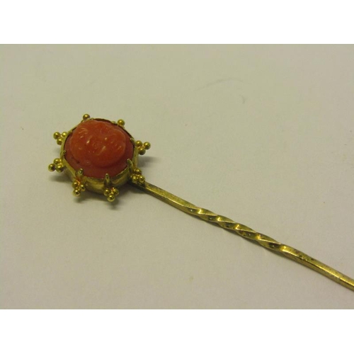 151 - An Edwardian gold stick pin with carved coral mask setting, 6cm l.