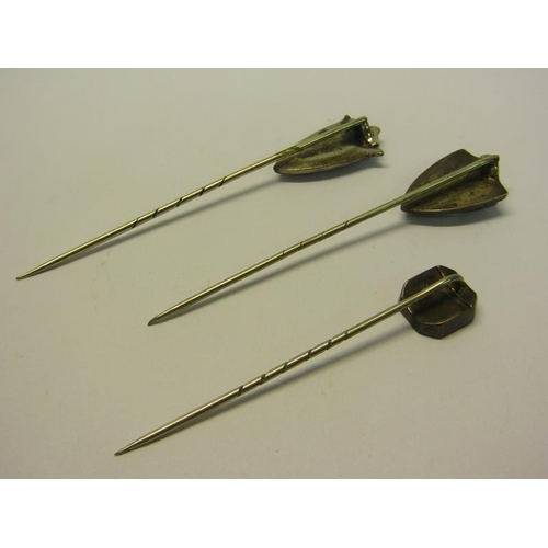 144 - A collection of three early 20c white metal stick pins, two of shield shaped form, all set with gree... 