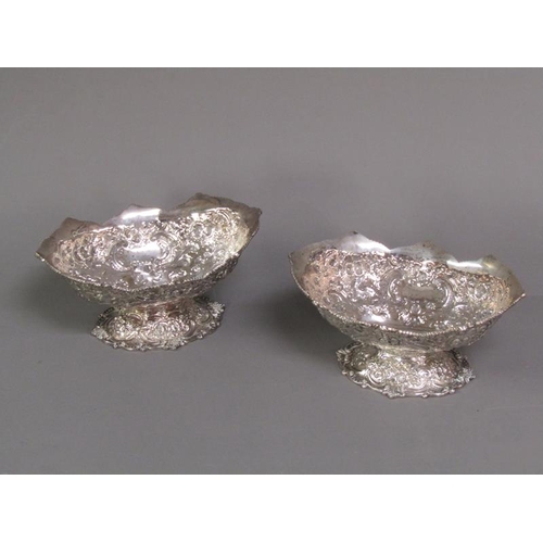 191 - A pair of late Victorian boat shapes bowls on stands with shaped upper rims, embossed and chased thr... 