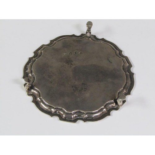 203 - A George II silver card tray of circular form with a raised and shaped border, supported on three ho... 