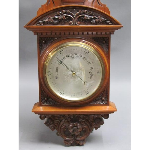 36 - An early 20c aneroid wall barometer, with 20cm diam. silvered dial set into a large heavily carved w... 