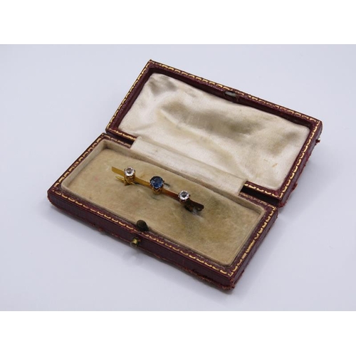 1593 - A gold bar brooch set with two cut diamonds flanking a central sapphire, 4cm w.