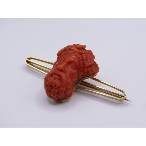 1596 - A 15ct gold bar brooch mounted with a carved coral Bacchus head, 7cm w.