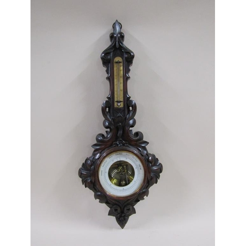 18 - An early 20c aneroid barometer in heavily carved mahogany case of wheel barometer shape.  The 13cm d... 