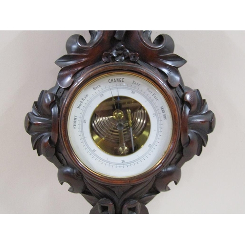 18 - An early 20c aneroid barometer in heavily carved mahogany case of wheel barometer shape.  The 13cm d... 