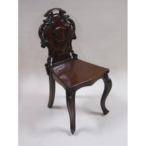 301 - A Victorian mahogany hall chair with a carved shield shaped back panel, solid seat and front slight ... 