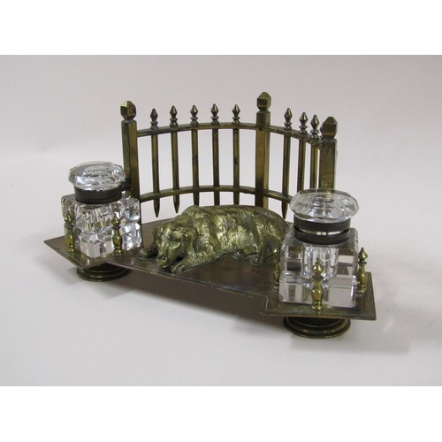 20 - An early 20c gilt metal two bottle inkstand formed as a lying dog backed by a curved fence and havin... 