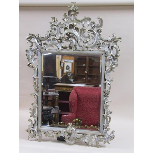 294 - A 19c style Florentine design silvered carved wood scrolling wall mirror,  137cm x 89cm overall.