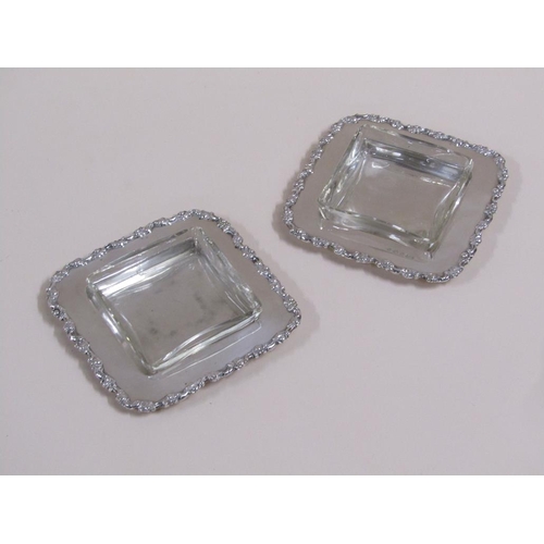 103 - A pair of Edwardian butter dishes of square form with cast scroll and leaf borders, with clear glass... 