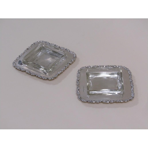 103 - A pair of Edwardian butter dishes of square form with cast scroll and leaf borders, with clear glass... 