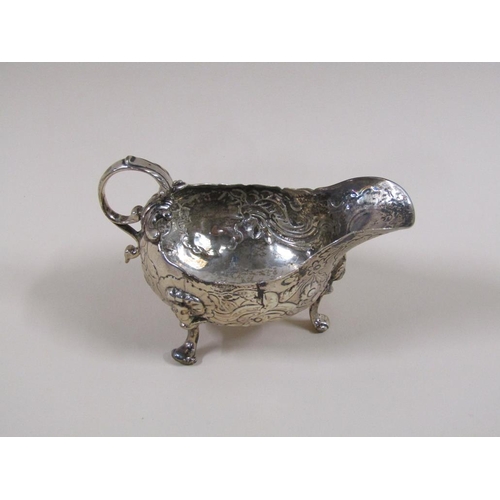 96 - An 18c silver sauce boat, embossed and chased throughout, supported on three legs with scroll handle... 