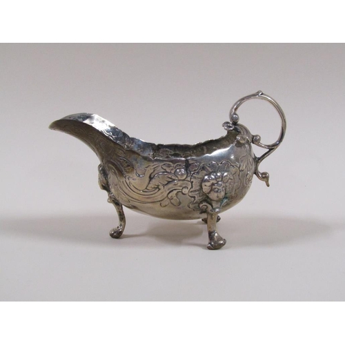 96 - An 18c silver sauce boat, embossed and chased throughout, supported on three legs with scroll handle... 