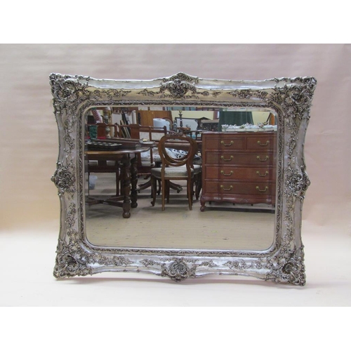 299 - A Georgian style silvered wall mirror of large proportion in a rococo style, embellished with flower... 