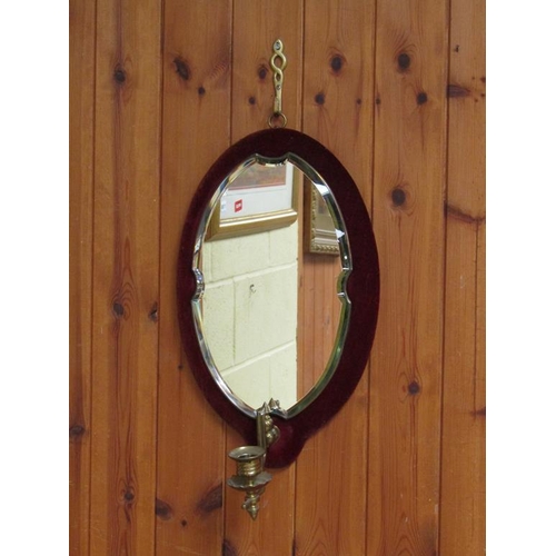 300 - A bevel edge oval wall mirror on a velvet pad with a brass sconce, 45cm x 25cm.