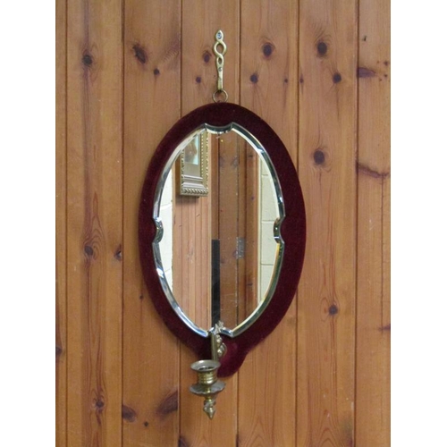 300 - A bevel edge oval wall mirror on a velvet pad with a brass sconce, 45cm x 25cm.