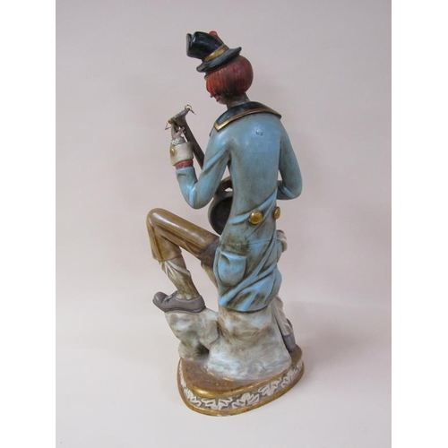 53 - An early 20c painted composite stoneware figure of a clown, seated, playing a string instrument, 81c... 