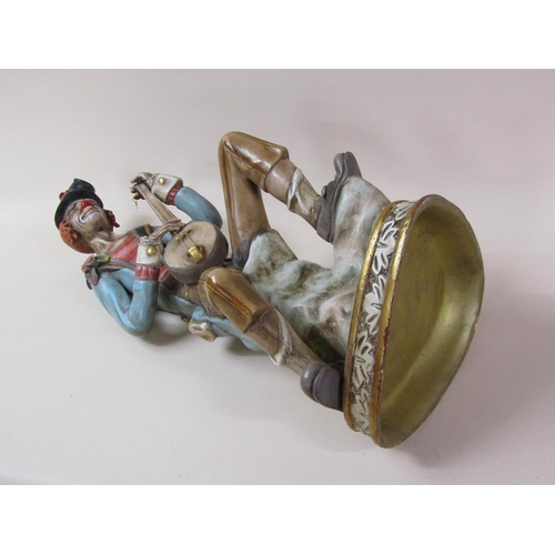 53 - An early 20c painted composite stoneware figure of a clown, seated, playing a string instrument, 81c... 