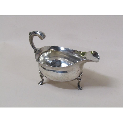 145 - A late Georgian silver sauce boat with open scroll handle, supported on three legs with hoof feet, m... 