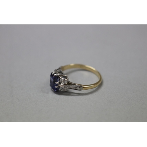 180 - 18ct white and yellow gold ring, claw set created emerald cut sapphire flanked by four round diamond... 