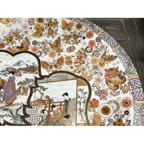 13 - Large Japanese porcelain charger, painted to the centre with leaf form panels, figures in outdoor an... 