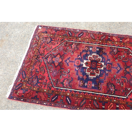 1063 - Handwoven red ground carpet, approx 130cm x 206cm