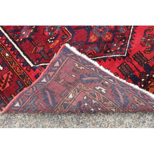 1063 - Handwoven red ground carpet, approx 130cm x 206cm