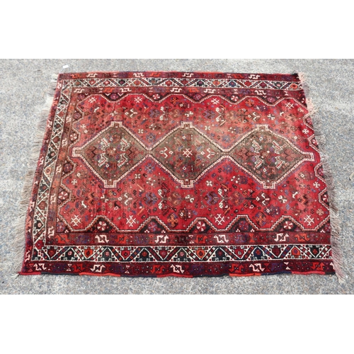 1215 - Persian handwoven wool carpet of red ground, with central diamond design, showing age & wear, cut do... 