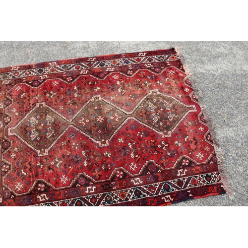 1215 - Persian handwoven wool carpet of red ground, with central diamond design, showing age & wear, cut do... 